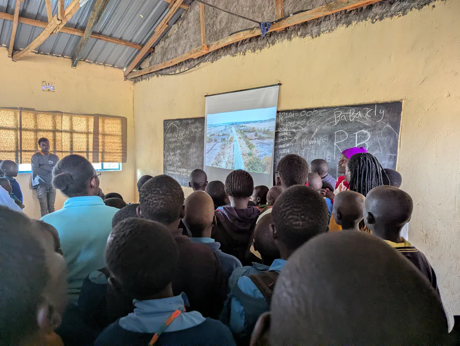 Pupils gathered close to a projector screen in a classroom, watching an image of the surrounding landscape.